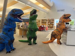 Photograph of staff in dinosaur costumes at the checkout counter in the library