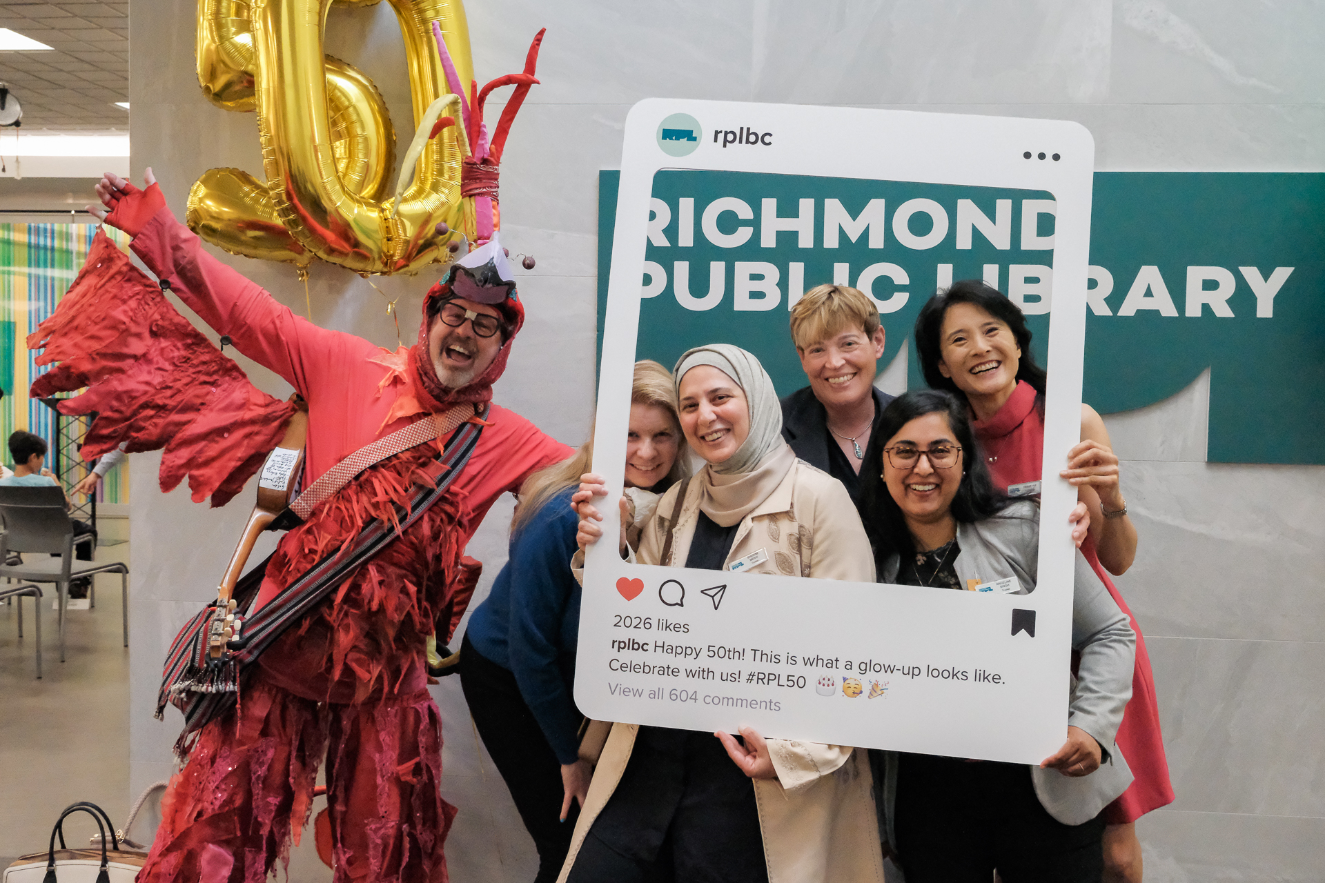 Photograph of 50th anniversary celebration, a diverse group of people stands together, proudly displaying a sign that reads "Richmond Public Library" in a friendly atmosphere.